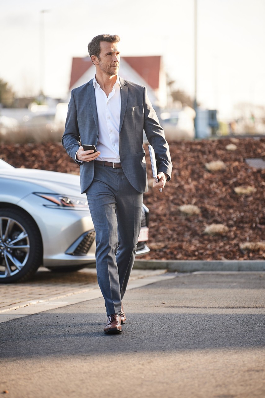 A person in a suit and tie walks with a cell phone, representing Lexus Business Leasing.