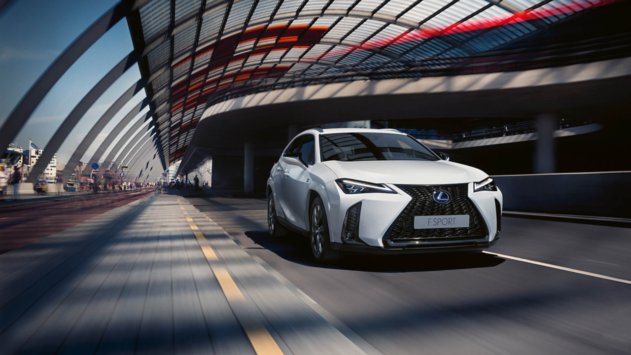 A white Lexus UX driving down a city street showcasing its sleek design and distinctive features.